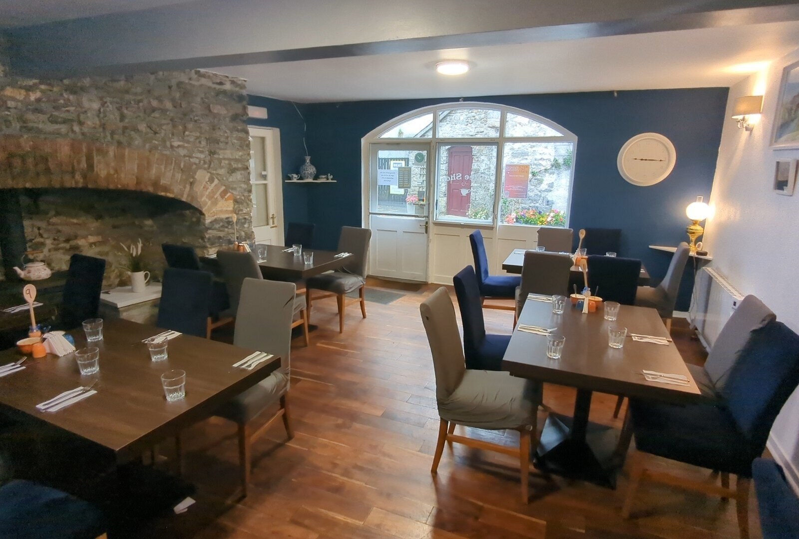 The back dining room at The Crank Café, with a stone fireplace, navy wall, and tables set for a sit-in